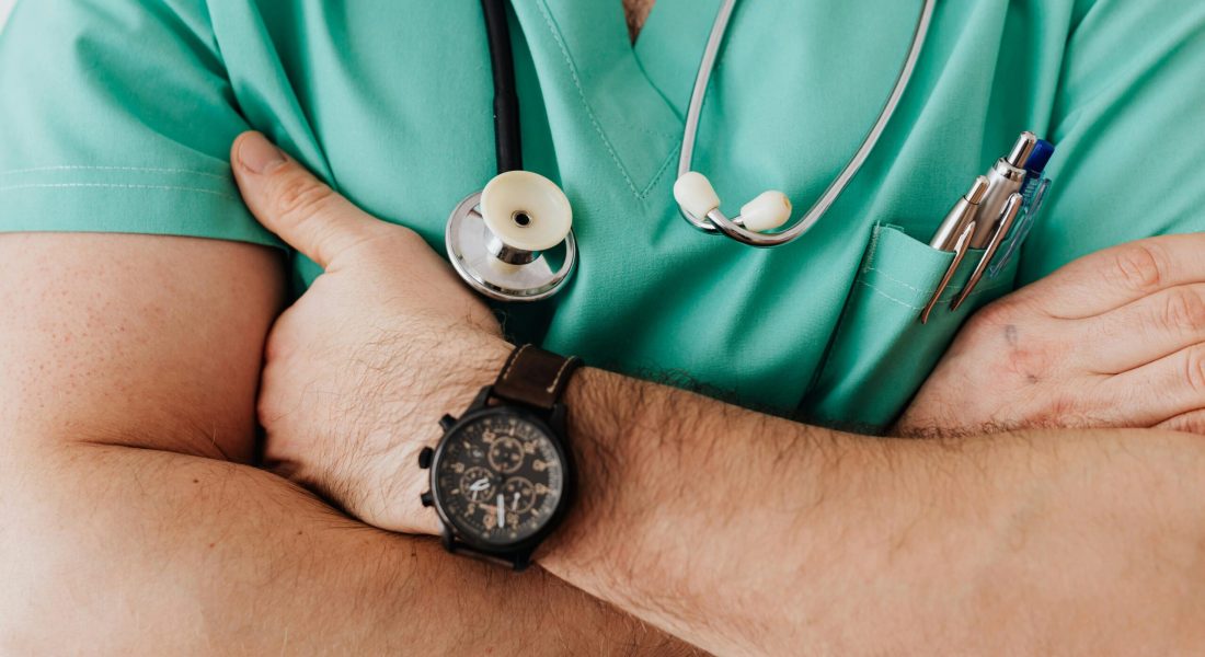 Close-up of a healthcare professional with arms crossed wearing medical scrubs and stethoscope.